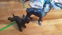 Two vintage cast iron dog door stops on wooden floor, showing size difference and wear.