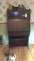 Full front view of the antique wooden secretary desk showing the glass paneled upper cabinet, drop front desk panel, and lower open compartment.