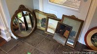 Photo showing all five items grouped on floor against a wall: three framed mirrors and two framed prints.
