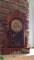 Front view of wooden gingerbread mantel clock showing carved scroll decorative top and base, clock face with roman numerals, and ornamental glass panel below dial.