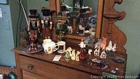 Photo showing a collection of wooden nutcrackers, two Christmas mugs, and various small decorative figurines all arranged on a wooden dresser.