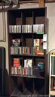 Wooden shelving unit with multiple rows of music CDs in jewel cases and some CD cover art visible including Mozart, Bach, Sinatra, Yo-Yo Ma, and Christmas-themed albums.