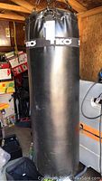 Full view of the black vinyl TKO punching bag hanging in a shed.