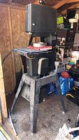 Full view of the 12in Craftsman bandsaw with metal stand inside a shed with various items around.