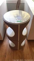 Single round mid-century modern style plastic end table, taupe base with circular cutouts and white top surface