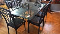 Full view of dining table with six black metal chairs with padded seats around it on hardwood floor.
