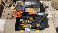 Photo showing the Mastercraft black plastic toolbox opened with visible contents including orange extension cord, Diesel angle grinder, work lamp, kneepads, and small hardware containers.