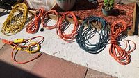Overview of 6 heavy-duty extension cords coiled and laid on ground, showing various lengths and colors (yellow, orange, green/blue).