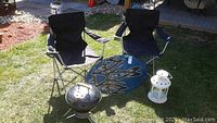 Two collapsible camp chairs, wakeboard behind them, portable Weber charcoal grill in front on the grass.