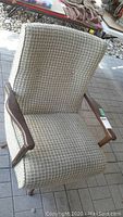 Front view of mid-century modern lounge chair showing tweed fabric upholstery and wooden armrests, placed outdoors on paved surface.