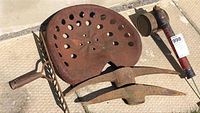 Overview of vintage iron tractor seat, pair of pickaxe heads, and vintage garden rake head, all showing rust and heavy use.