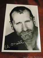 Full photo of Ed O'Neill black and white signed 5x7 photo on a reddish surface.