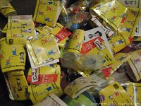 Sealed miniature bobble head figures of The Simpsons characters along with their yellow paper inserts showing character illustrations and info, grouped together on a surface.