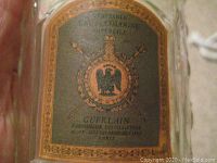 Close-up of bottle front label showing green label with gold border, eagle crest, crown, crossed scepters, and text.