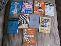 All eight basketball rule manuals displayed on fabric with various colors and designs.