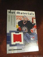 Front close-up of 2005-06 Fleer Hot Prospects Hot Materials hockey card featuring Henrik Lundqvist with red fabric swatch.