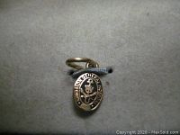 Front view of small oval gold charm with Kingston General Hospital inscription and anchor emblem