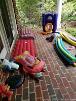 View of assorted pool toys including inflated rafts, Sit 'n Floats and pool noodles laid out on brick porch.