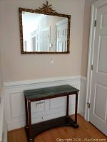 Wall mirror in ornate gold frame hanging above the wooden hall table with green marble top