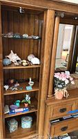 Wooden cabinet shelves holding rocks, shells, figurines, faux flowers beside mirrored door with bottom storage