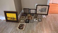 Multiple small to medium framed artworks, vintage booklets, and empty picture frames arranged on floor
