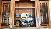 Wooden shelf with cat-themed decorative plates and figurines, including a white cat with blue bow and ceramic containers