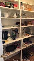 White Corelle plates and bowls, plastic tumblers, jars and metal tins seen on shelves.
