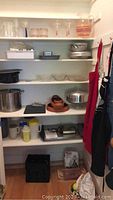 Pantry shelves with assorted bakeware, cookware, drinkware, aprons, and kitchen accessories