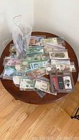 Wide shot of assorted world banknotes, coins in plastic bags laid out on a round wooden table.