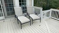 Two metal and fabric lounge chairs on a deck near glass doors.