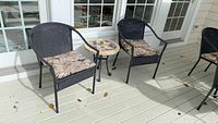 Patio chairs and tile top side table all positioned on an outdoor painted wood deck in front of glass doors.