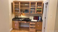 Full view of a built-in wooden office desk with shelves holding various office items and a desk lamp