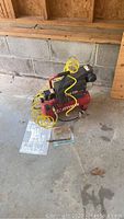 Craftsman air compressor in a garage setting with yellow coiled air hose attached, parts and manual nearby on floor.