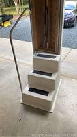 Front view of single white plastic dock step with three black non-slip strips on treads and attached metal handrail.