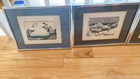 Front view of two framed Japanese scene prints showing nature and village scenes in neutral tones.