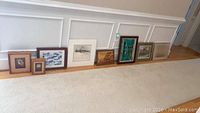 Eight framed art pieces and shadow boxes lined up on floor showing variety and sizes