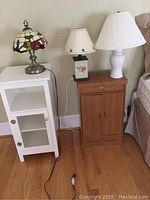 Three table lamps and two pieces of furniture (night stand and Hindu altar cabinet) arranged side by side against wall near bed.