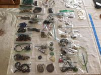 Overview of multiple clear plastic bags with various necklace and pendant pieces laid on fabric surface