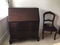 Front view of wooden secretary desk with drop-down writing surface and drawers.