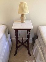 Full view of antique side table with white marble top, placed between two beds with cream ceramic lamp on top.