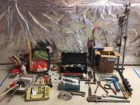 Overall display of painting brushes, hand tools, caulking gun, safety goggles, pliers, hammer, and a toolbox in background