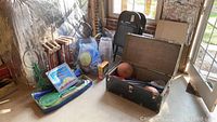 Overview of all items grouped together including croquet set, rackets, steamer trunk open with balls inside, and folding chairs in background.