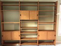 Front view of fully assembled modular teak wall unit showing adjustable shelves and sliding-door cabinets