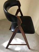 Side angle view showing teak frame, angled legs, curved backrest and upholstered seat