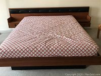 Full front view of teak platform bed with mattress and integrated headboard and side tables