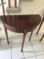 Front angle view of half moon table showing wood finish, turned legs, and decorative medallion on corner.