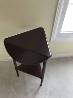 Photo showing the table from a top angle, displaying the triangular top with three edges joined and dark wood finish.