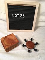 Teak candle holder with steel prongs alongside stacked teak coasters and LOT 35 sign