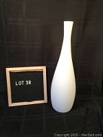 Full view of tall white tapered vase next to lot number board