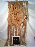 Full view of large tan and cream macrame wall hanging with wood beads and abstract knotting, mounted on wooden dowel